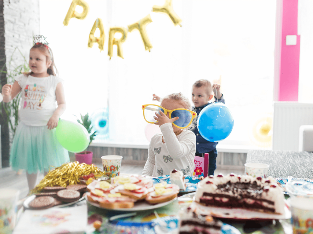 الأطفال يستمتعون بحفلة عيد ميلاد مع بالونات، نظارات كبيرة مضحكة، وطاولة مليئة بالحلويات.