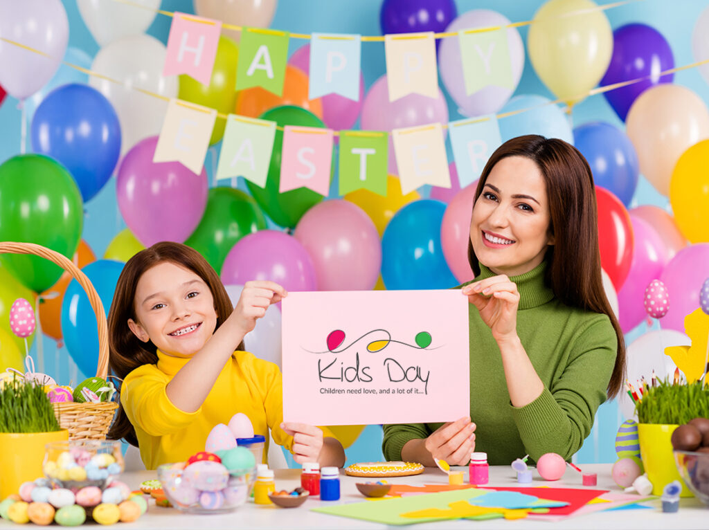 Mother and daughter enjoying arts and crafts at a festive Kids Day event, surrounded by colorful balloons and Easter-themed decorations.